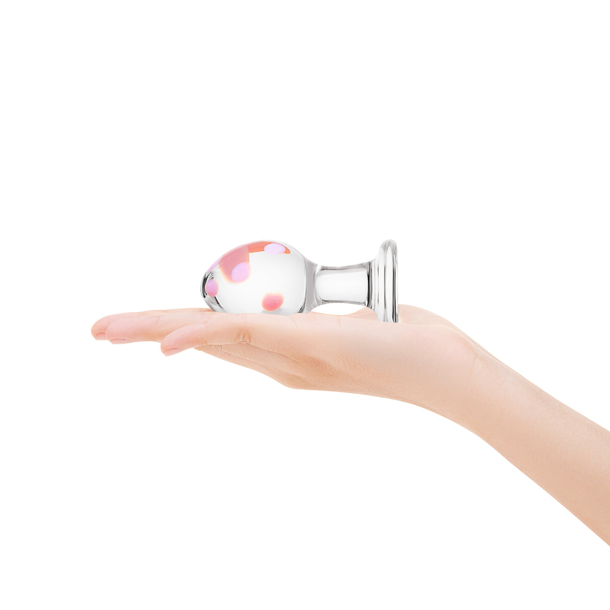 Anal glass plug with pink polka dot design held in a hand on a white background