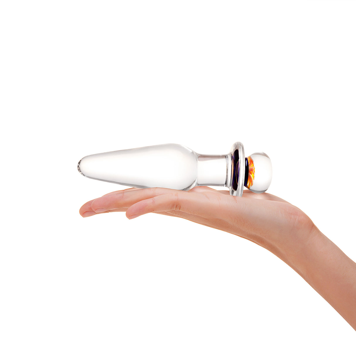 Glass anal plug with slim tapered tip and flower design on the base held in a hand on a white background