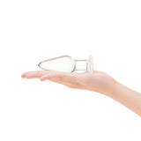Clear glass anal plug with taoered tip and flared bottom held in a hand on a white background