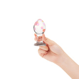 Hand holding a glass anal plug with a polka dot pattern on a white background