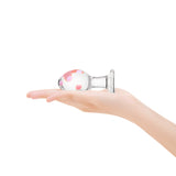 Anal glass plug with pink polka dot design held in a hand on a white background