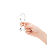 Hand holding a clear glass anal plug against a white background
