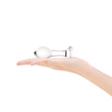 Clear glass anal plug held in a hand against a white background