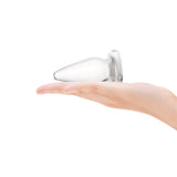 Clear glass cone-shaped anal plug held in a hand against a white background