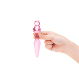 Hand holding a Pink glass anal plug with a bear-shaped base and tapered smooth tip against a white background