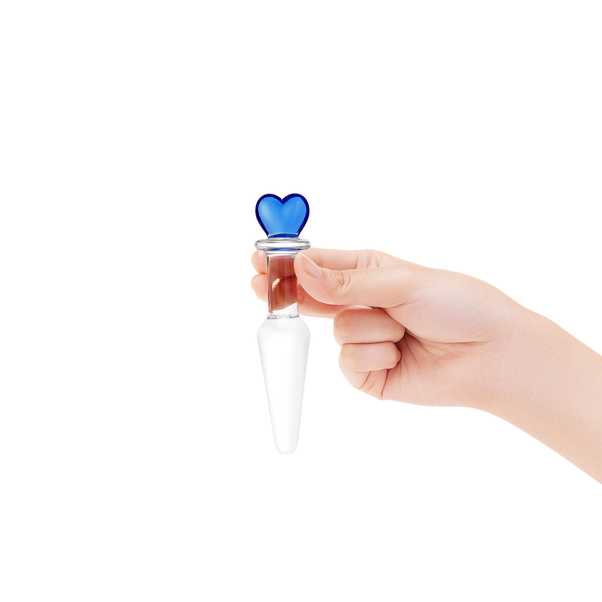 Hand holding a clear glass butt plug with a blue heart-shaped base, slim neck and smooth tapered tip on a white background