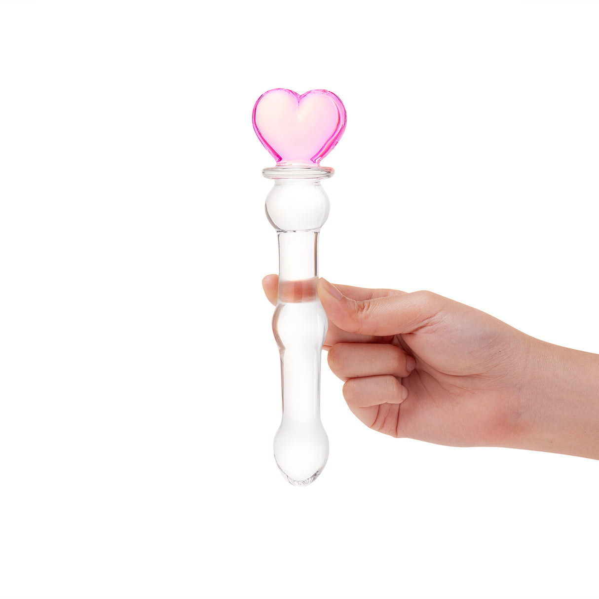 Hand holding a beaded glass dildo featuring a pink heart base and mid-shaft bead on a white background