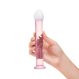 Hand holding aglass anal plug featuring a blush-pink shaft and frosted white tip with bubble-accented shaft  on a white background
