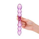 Hand holding apurple dual-ended glass dildo with beaded tips and rippled center against a white background