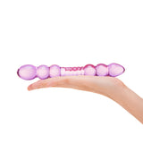 purple dual-ended glass dildo with beaded tips and rippled center held in a hand on a white background