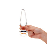 Hand holding a Glass anal plug with slim tapered tip and flower design on the base against a white background